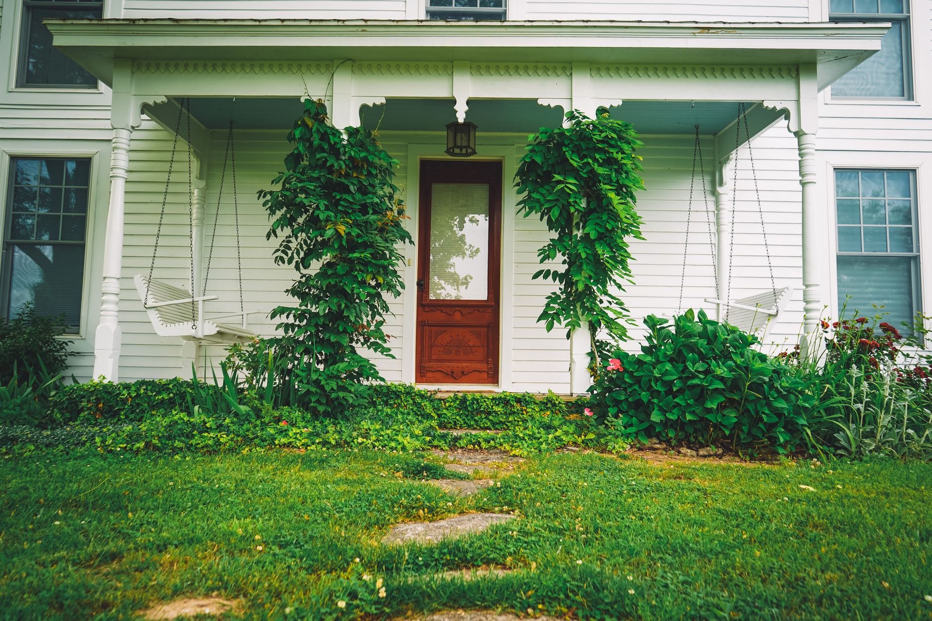Inviting front porch of a white craftsman house with vibrant plants and porch swings